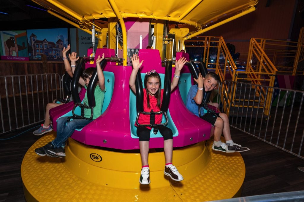 kids with their hands up on a yellow spinning ride at the funplex east hanover