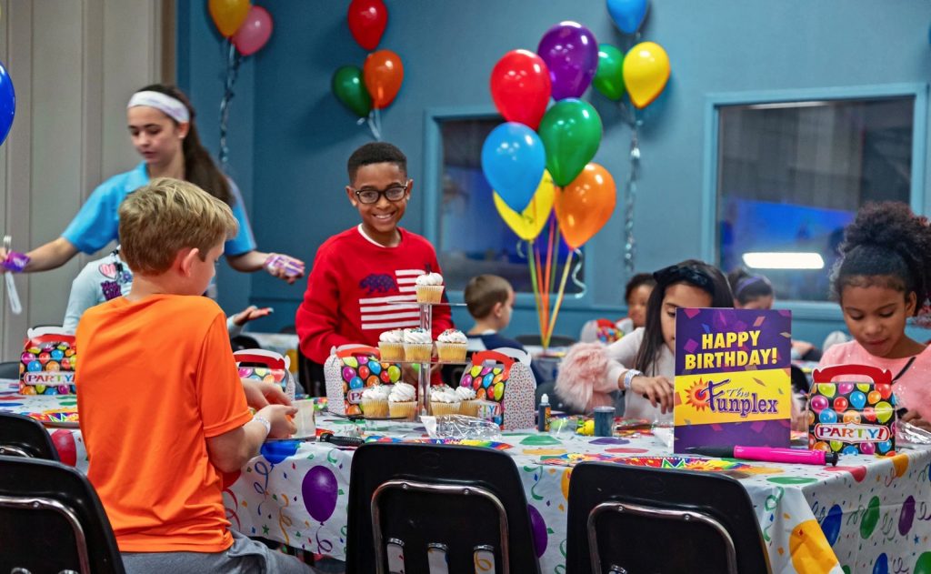 group of smiling kids celebrating an indoor birthday party at The Funplex Mount laurel with balloons, cupcakes, and decorations